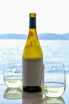 A bottle of white wine with two glasses outside at a lake during a summer vacation. The drink is refreshing and cool during  a hot sunny day. 