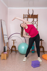 Middle aged woman does side bends with her arm raised during fitness exercise at inside home. Full...