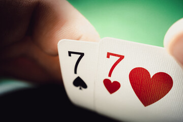 A pair of sevens in a man's hand close up, poker background. Seven of hearts and seven of spades.