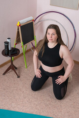 Adult woman is sitting on floor with her knees bent and hands resting on her hips. She is engaged...