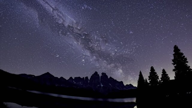 Milky Way arches over a tranquil mountain lake, reflecting starlight and silhouetted trees. A breathtaking nightscape