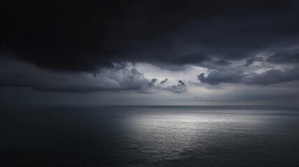 Dark storm clouds gather over a calm sea, with a patch of light reflecting on the water's surface, creating a dramatic and moody atmosphere.