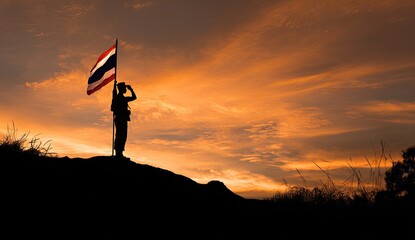 Silhouette of soldier saluting Thai flag at sunset