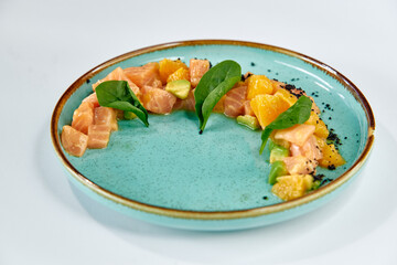 A Vibrant Dish of Fresh Salmon Cubes Accompanied by Zesty Orange Segments and Fresh Spinach Leaves on a Beautifully Crafted Turquoise Plate