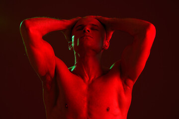 Strong man posing dramatically under bright red lights, showcasing his muscular physique. This...