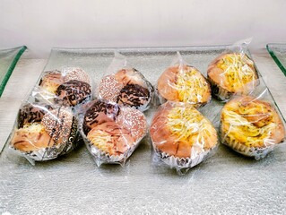 Assorted sweet & savory buns in clear packs on glass tray. Delicious bakery treats
