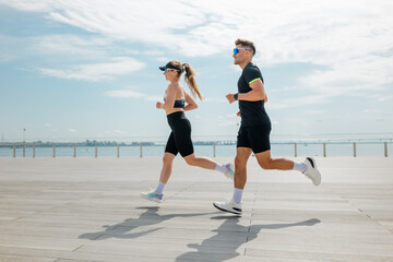Couple jogging along a waterfront promenade in sunny weather