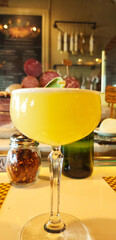 Close-up image of a vibrant Amalfi cocktail, crafted with tequila, Cointreau, sage nectar, fresh lime, and pineapple, topped with a delicate foam layer. The golden drink is served in an elegant glass