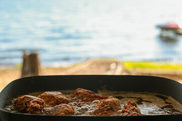 Homemade crispy fried chicken cooking in hot oil for a lake picnic lunch or dinner. Delicious food being cooked outside in a skillet.