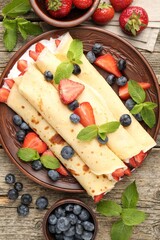 Tasty crepes with berries, cream and mint on wooden table, flat lay
