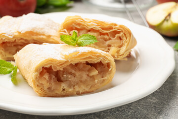 Pieces of tasty apple strudel with powdered sugar and mint on grey table, closeup