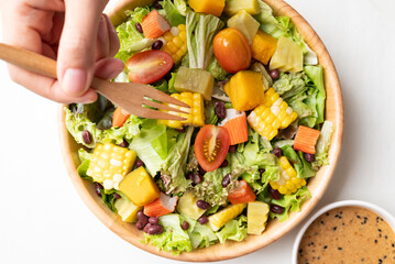 Top view of colorful vegetable salad in wooden bowl with Japanese sesame dressing on white background, Healthy, fresh, plant based eating concept