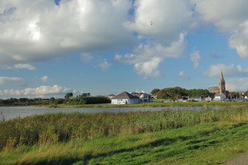 Scenic Irish Village with Historic Church Tower, Tranquil Lake and Grassy Path Under Blue Sky and...