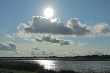 Bright Sun Over Tranquil River Landscape with Dramatic Clouds and Reflections – Peaceful Rural Countryside Scene with Blue Sky and Silhouetted Horizon, Ideal for Nature and Travel Concepts
