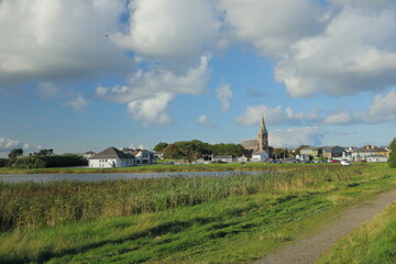 Scenic Irish Village with Historic Church Tower, Tranquil Lake and Grassy Path Under Blue Sky and...