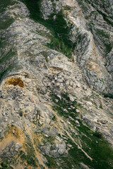 Rocky hillside with scattered boulders and patches of green grass, showcasing natural geological formations and textures in a mountainous landscape