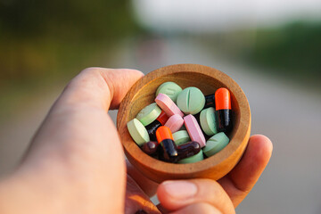 Conceptual image of healthcare and medicine, with a hand holding a bowl of various colorful pills...