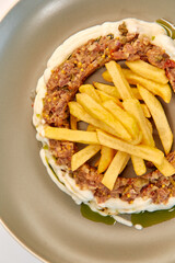 A Gourmet Dish Featuring Layers of Savory Meats Surrounded by Creamy Sauce and Accompanied by Golden French Fries Artfully Arranged on a Plate