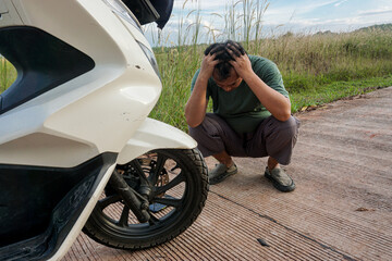 Travel mishap and transportation trouble concept. A frustrated man with his head in his hands after his scooter broke down on a rural road.