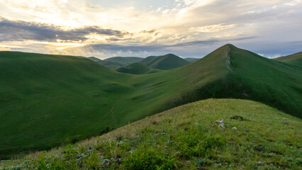 Expansive green hills under a dramatic sky at sunset, showcasing rolling landscapes and vibrant vegetation, creating a serene and tranquil natural environment