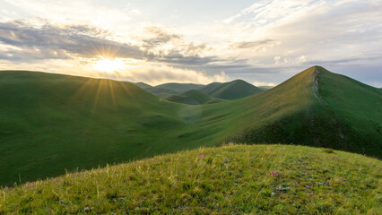 Expansive green hills under a dramatic sky, with sunlight breaking through clouds, creating a serene landscape that captures the beauty of nature and tranquility in the countryside