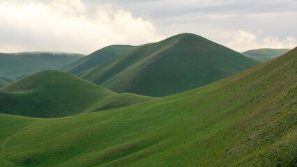 Rolling green hills under a cloudy sky create a serene landscape, showcasing the beauty of nature and the tranquility of the countryside in a peaceful environment