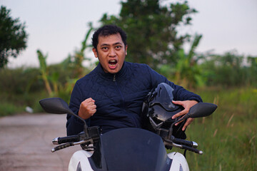 Triumphant young motorcyclist shouting with joy and raising a fist after a successful ride outdoors.