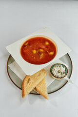 A Delicious Bowl of Tomato Soup Served with Soft Dumplings and Accompanied by Crispy Toast and a Side of Creamy Dip for a Perfect Appetizing Meal Experience