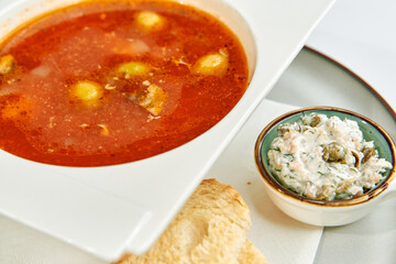 A hearty bowl of rich tomato soup accompanied by a creamy spread and a side of crispy bread, perfect for a comforting meal any day.