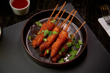 Savory Skewered Delights: Crispy Fried Appetizers Garnished with Fresh Herbs and Accompanied by a Tangy Dipping Sauce for a Flavorful Experience