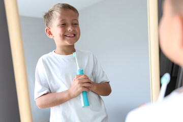 Cheerful young boy brushing teeth in bathroom. Morning hygiene routine, dental care and healthy...