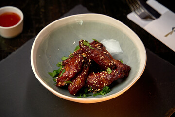 Deliciously Spicy Glazed Chicken Wings Garnished with Fresh Herbs and Sesame Seeds in a Contemporary Bowl Setting