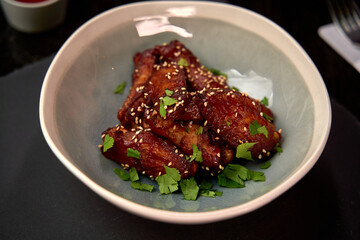 A Close-Up of Crispy Chicken Wings Garnished with Fresh Herbs and Sesame Seeds in a Stylish Bowl on a Dark Surface
