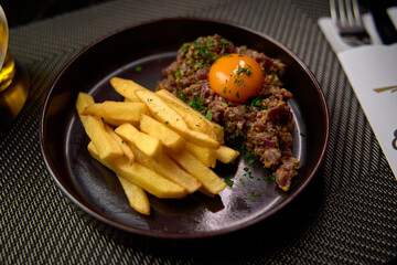 A delectable dish featuring finely minced meat topped with a bright yolk and accompanied by crispy golden fries, perfect for a savory meal experience.