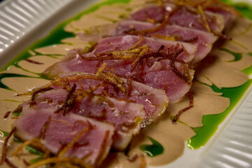 Sliced Gourmet Dish Featuring Delicately Prepared Fish with Crispy Garnish and Flavorful Sauce, Artistically Plated for Exquisite Dining Experience