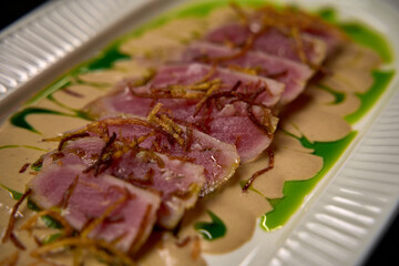 A Delicate Dish Featuring Slices of Tuna Accompanied by a Rich Sauce and Garnished with Crispy Fried Onions Creating a Beautiful Presentation