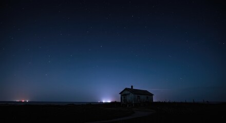 Obraz premium A solitary, weathered house stands on a dark beach under a star-studded night sky