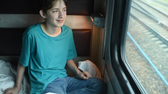 A 12 year old boy sits by the window on a long-distance train in summer.	