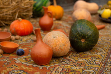 Tasty ripe fresh juicy yellow pumpkin, melon, ceramic wine decanter, clay jug on ethnic carpet at...