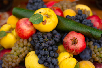 Horizontal photo. Tasty ripe fresh juicy fruit plate with red pomegranate, plum, yellow apple, pear, grape. Vegetable counter stall at street farm market on harvest autumn fall city holiday Tbilisoba