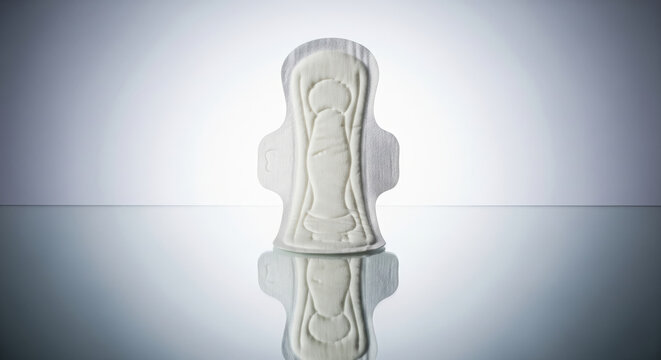 Clinical and minimalist still life of a sanitary pad standing upright with a reflection on a grey background
