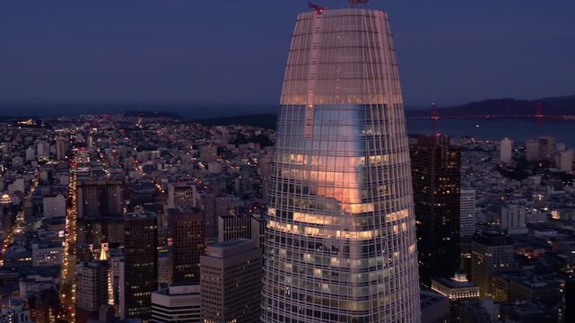 Night view of the Salesforce Tower in San Francisco, California, USA. The city lights illuminate the building as dusk settles over the urban landscape.