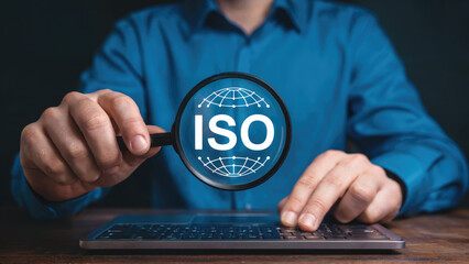 ISO certification expert verifying global quality standards with magnifying glass on laptop keyboard