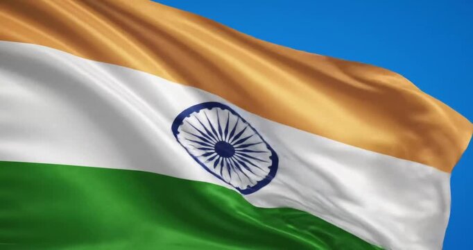The Indian flag with a gold pole flutters majestically under the blue sky.