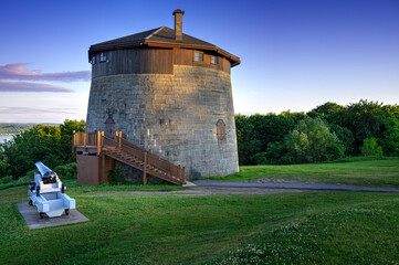 Historic Martello tower on the Plains of Abraham in Quebec City, captured at sunset with a cannon in front. Ideal for themes of military history, tourism, heritage, and scenic architecture.