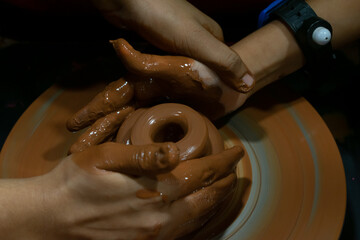 A picture of hands of a child and a teacher teaching pottery showing education, self development,...