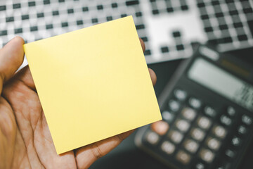 Hand holding Blank Sticky Note on Keyboard and Calculator. Forecast for finances . Money, Budget, tax, investment, financial and savings. Copy space.