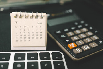 Calendar of July 2025 with Calculator and Keyboard on Office Desk. standing desk calendar showing the month of July 2025. planning, finance, budgeting, deadlines, and office organization.