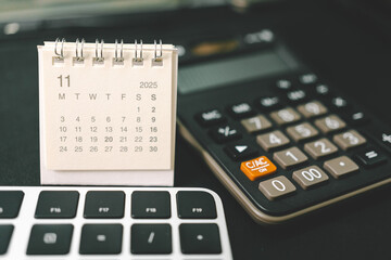 Calendar of November 2025 with Calculator and Keyboard on Office Desk. standing desk calendar showing the month of NOV 2025. planning, finance, budgeting, deadlines, and office organization.