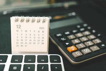 Calendar of DECEMBER 2025 with Calculator and Keyboard on Office Desk. standing desk calendar showing the month of DEC 2025. planning, finance, budgeting, deadlines, and office organization.